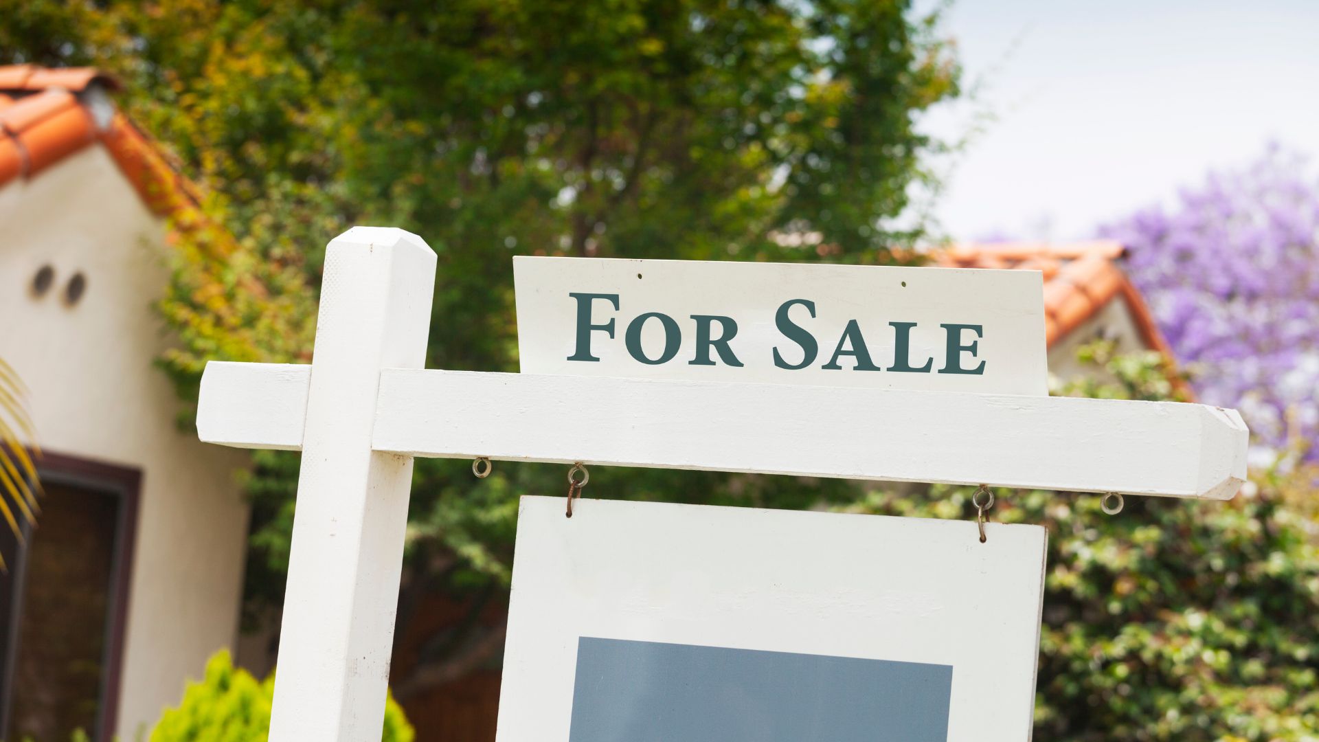 White for sale sign in front of house with garden and trees