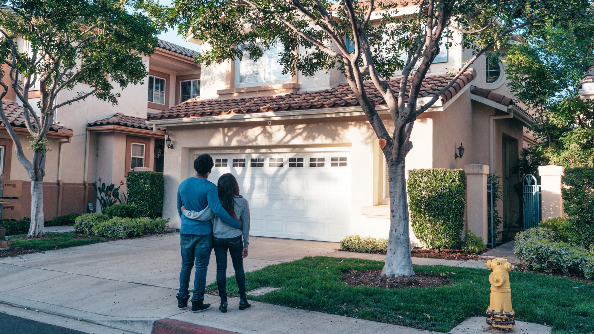 Couple standing in front of suburban house with white garage and trees