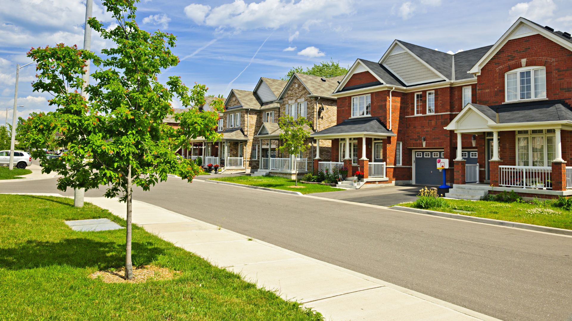 Suburban street with brick houses, green trees, and neatly trimmed lawns