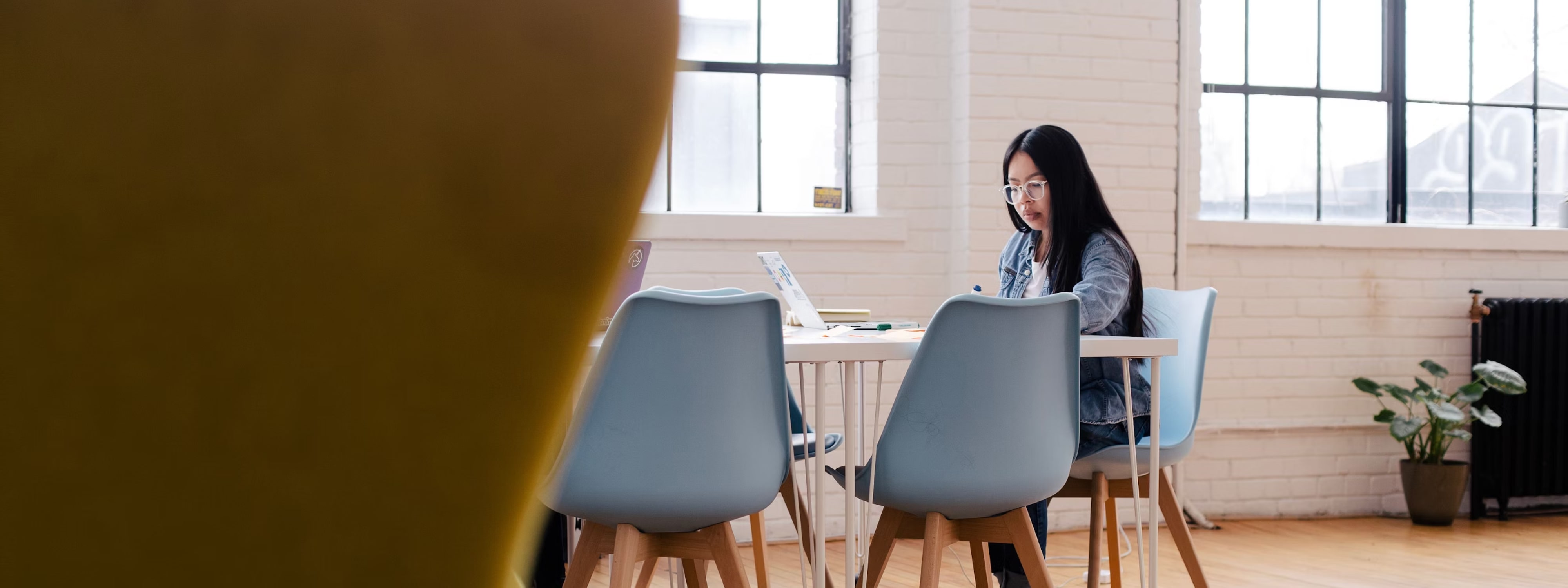 Woman working on laptop in bright, minimalist office space with blue chairs