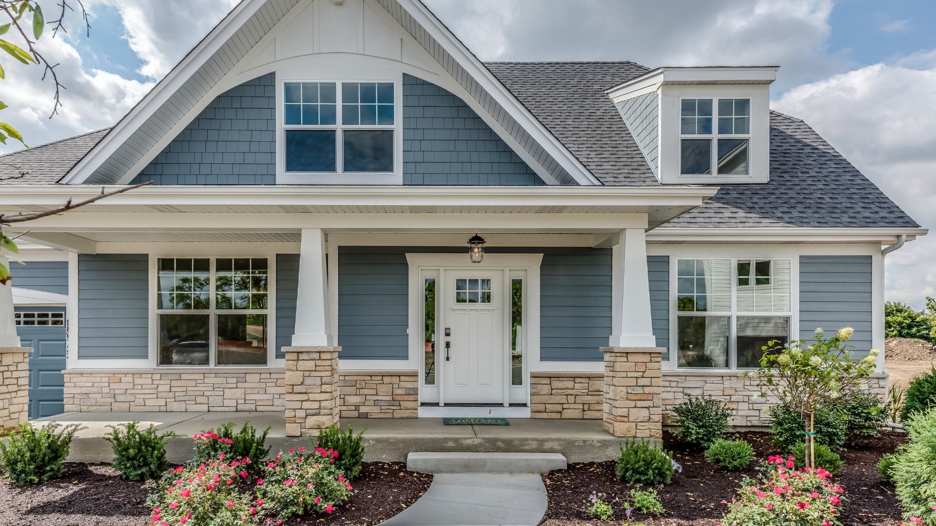 Blue craftsman-style house with stone foundation and colorful garden landscaping