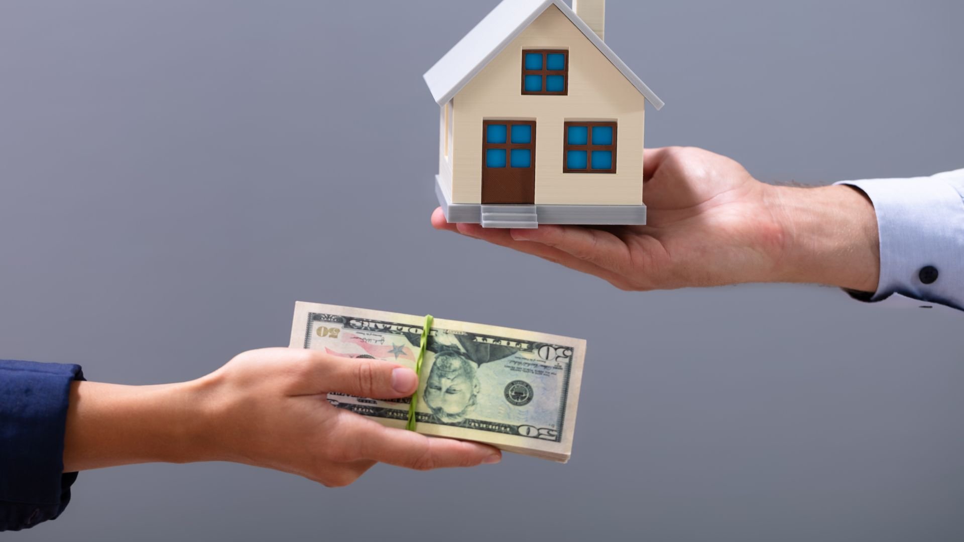 Hand exchanging money for miniature house, representing real estate transaction