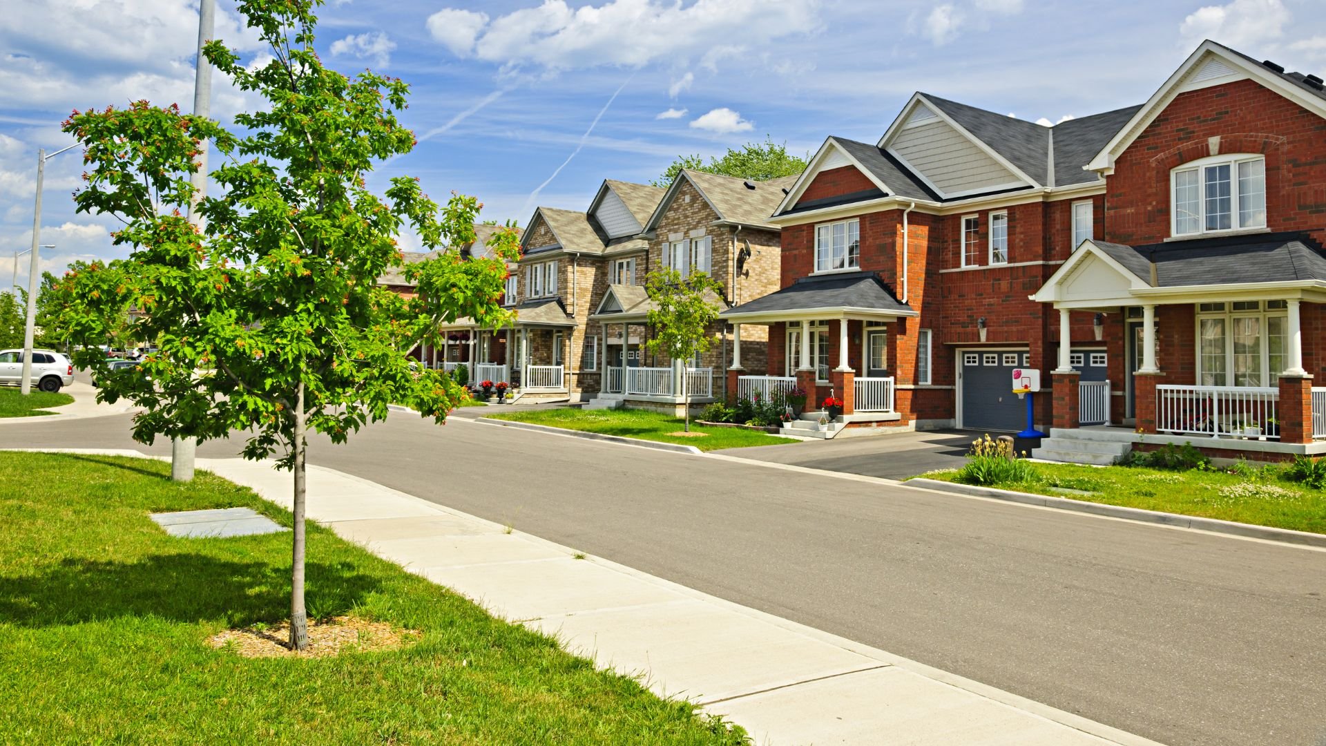 Suburban street with brick houses, green lawns, and young trees