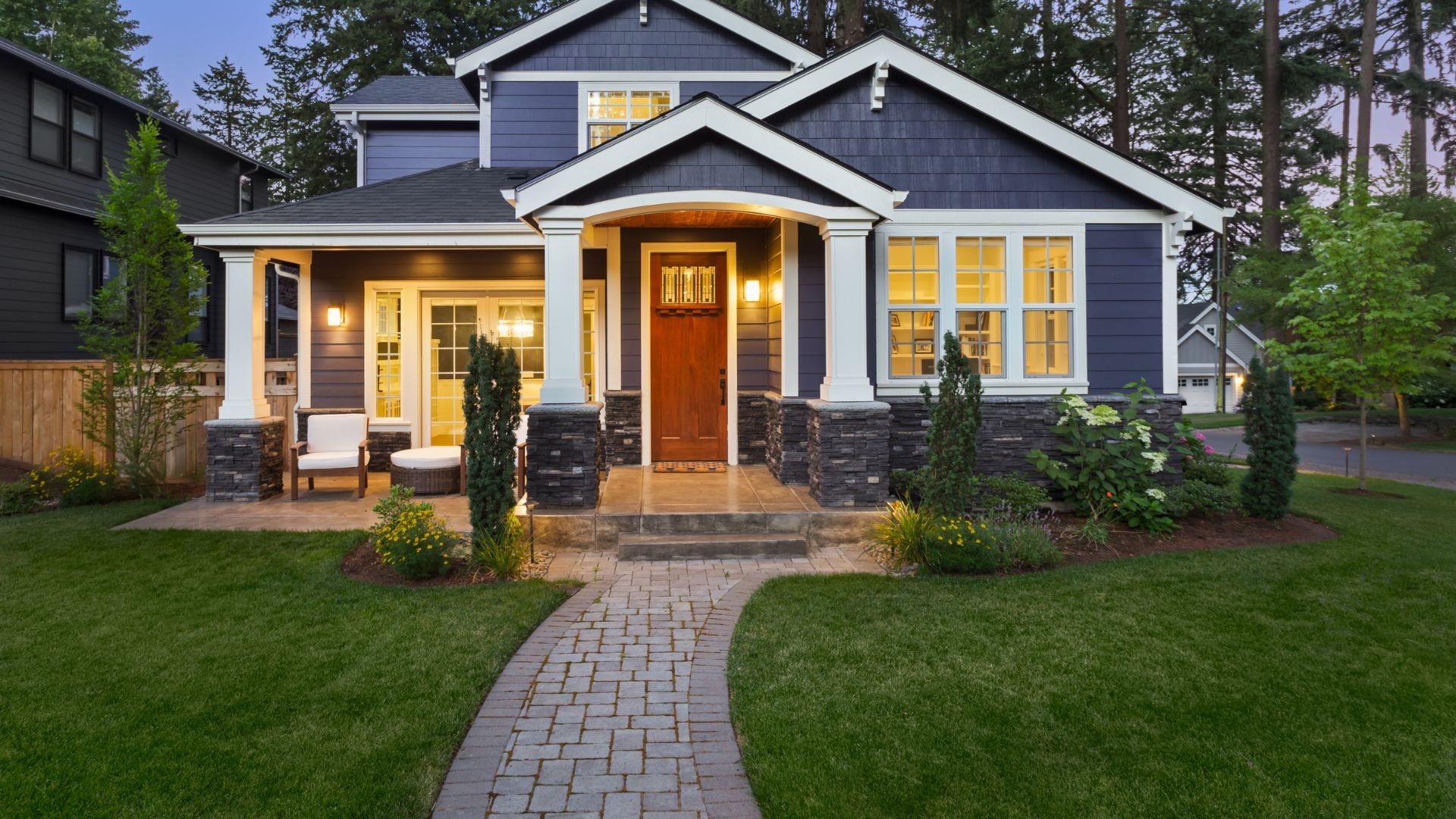 Blue craftsman-style house with stone columns and warm evening lighting